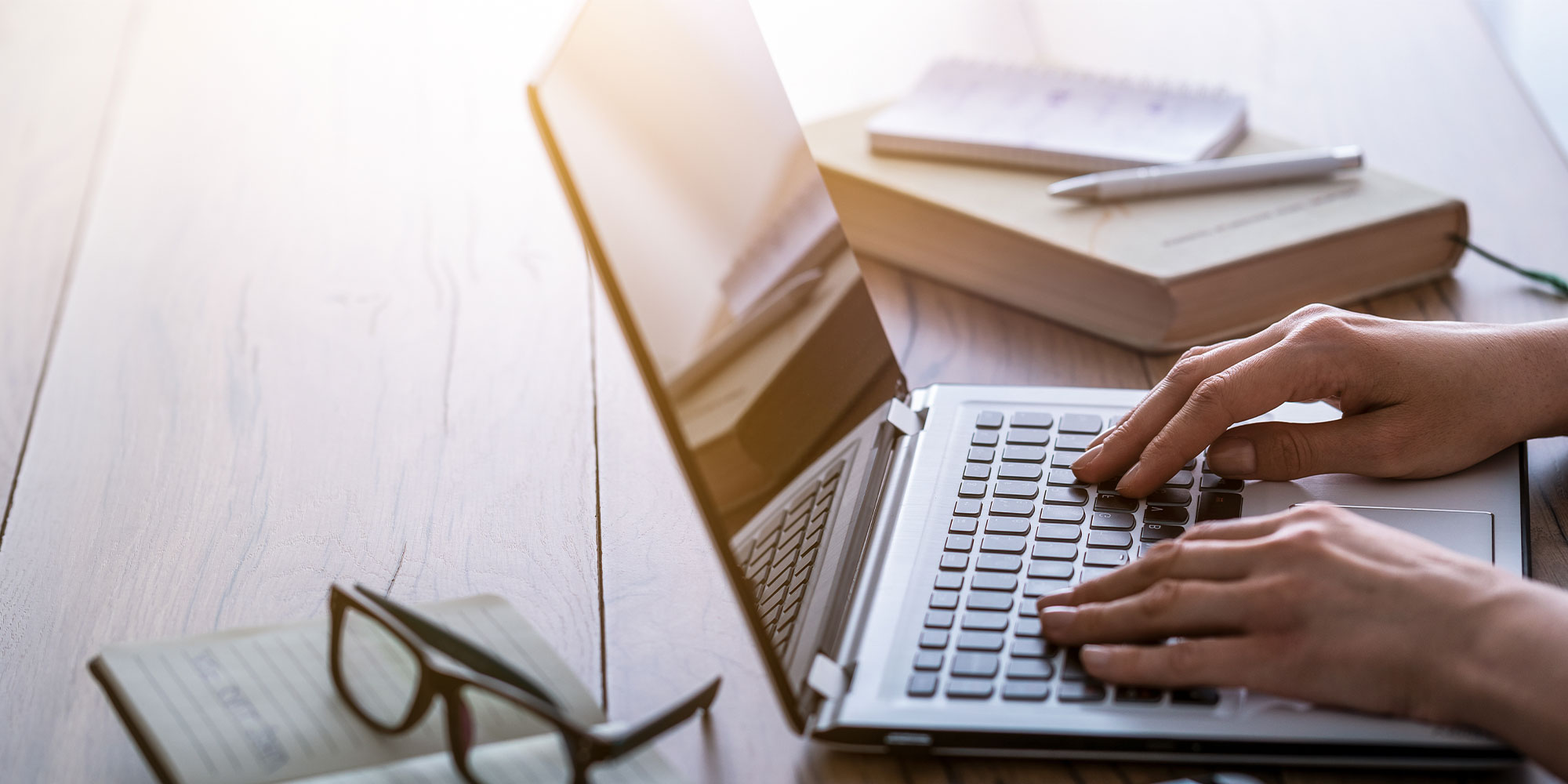 person using computer with books and glasses in background